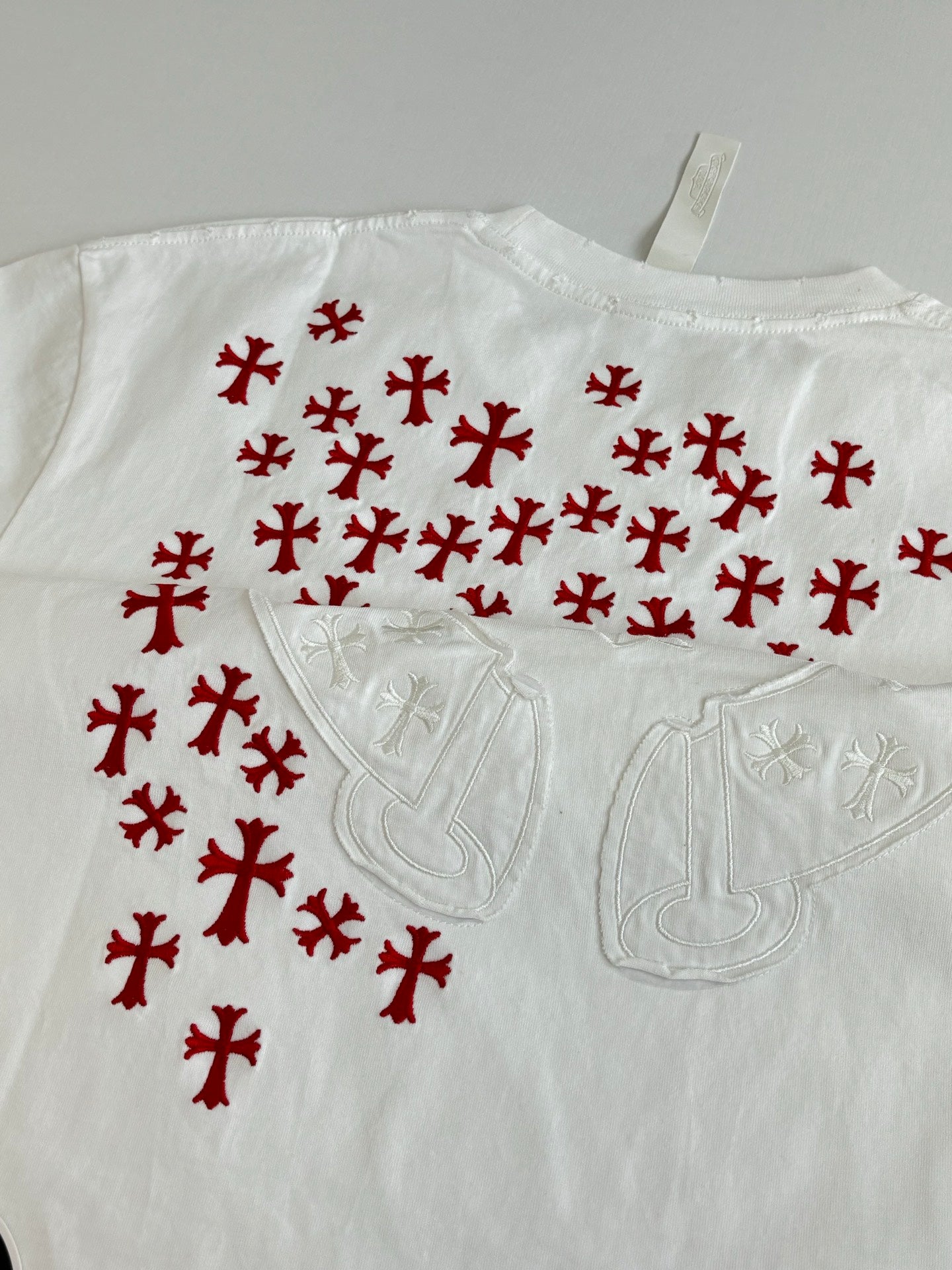 White T-shirt close-up with red pattern and embossed chest emblem detail