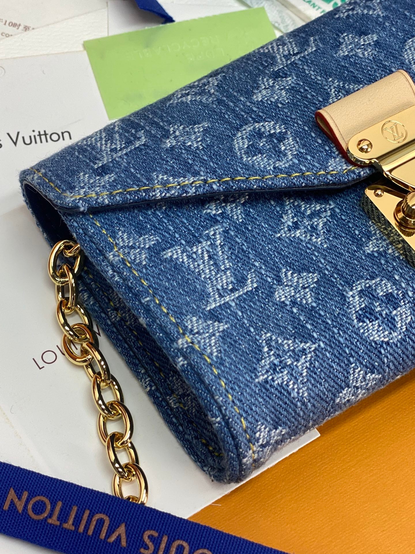 Close-up of blue monogram flap bag with gold clasp plate and chain