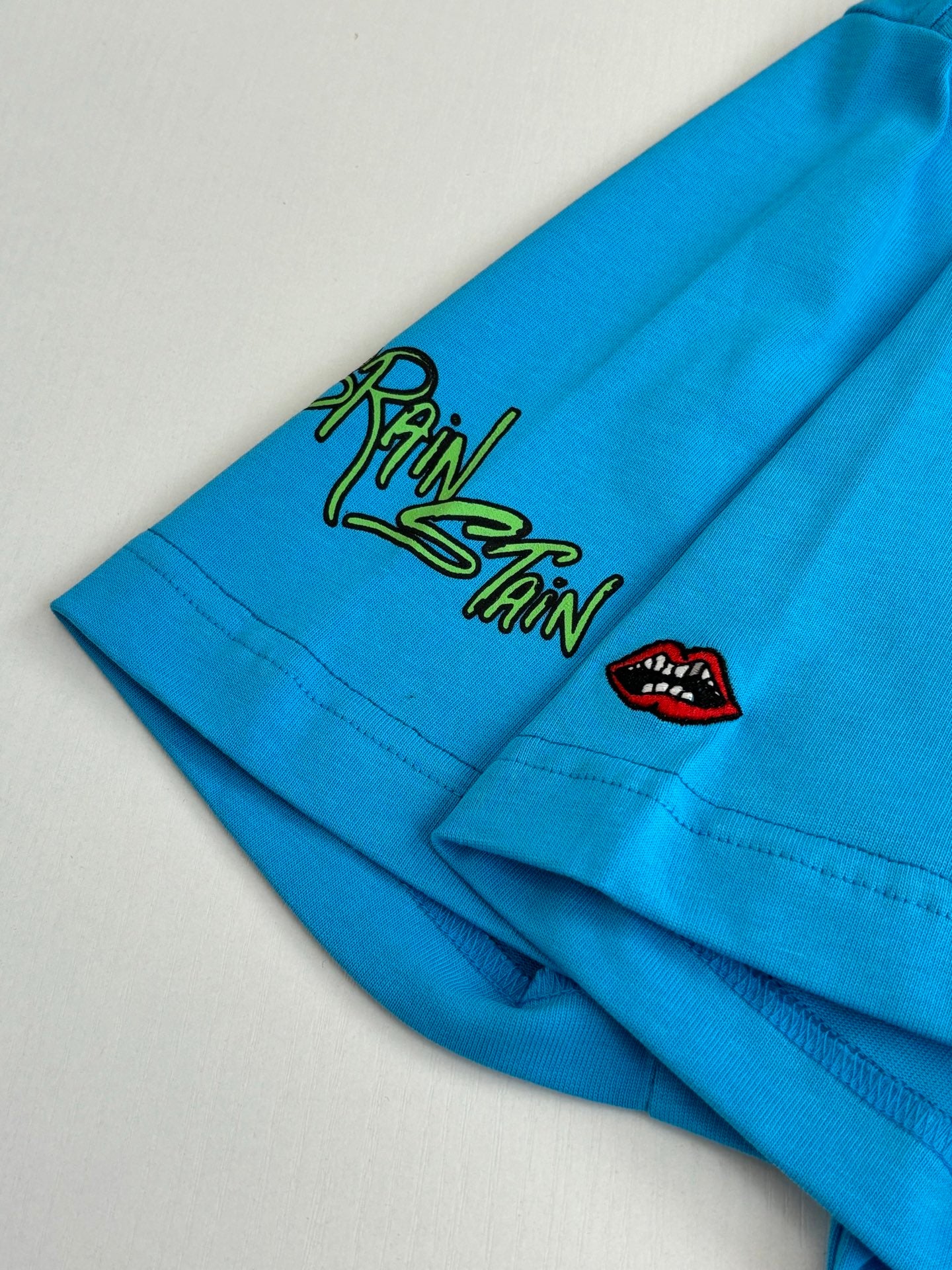 Blue T-shirt sleeve with small green doodle graphic and red lip icon