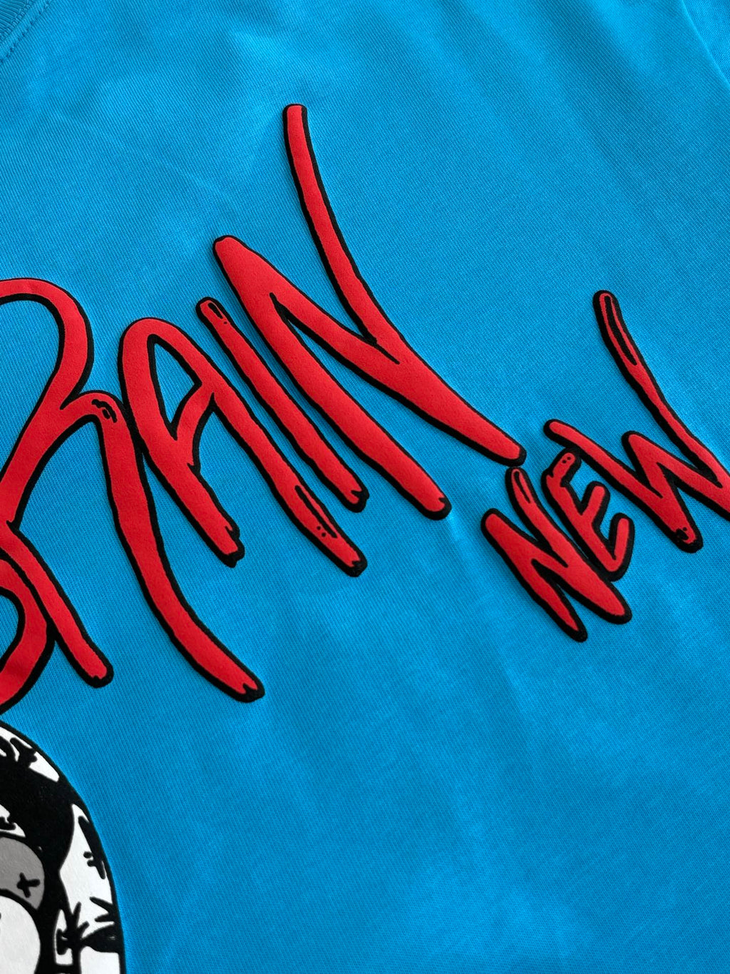 Blue T-shirt close-up of red “BRAIN NEW” graphic lettering