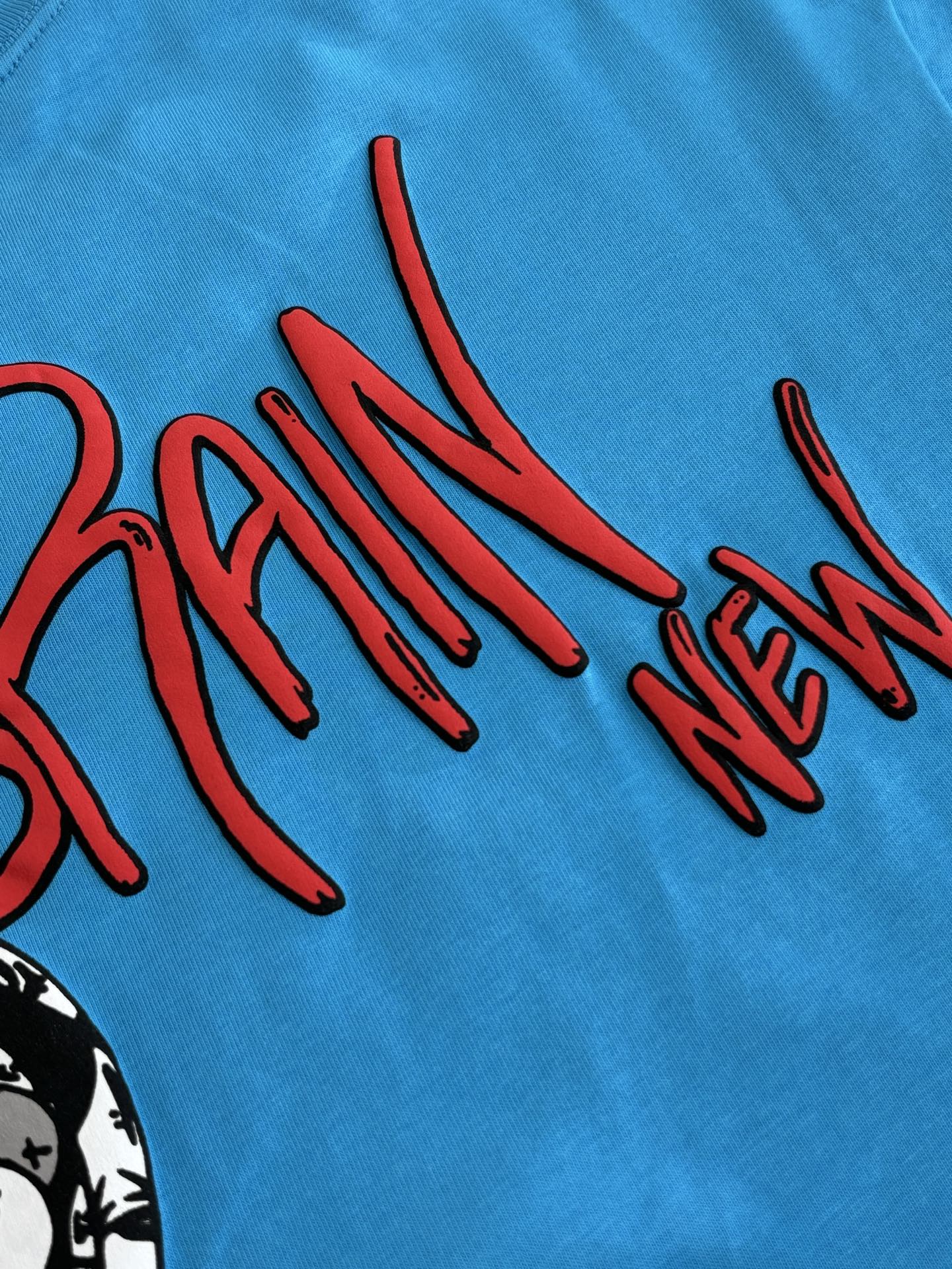 Blue T-shirt close-up of red “BRAIN NEW” graphic lettering