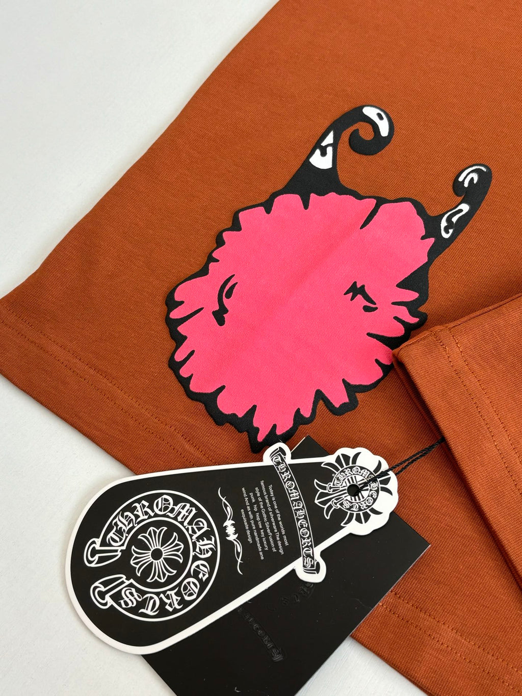 Orange T-shirt with large pink character graphic and attached black hang tag