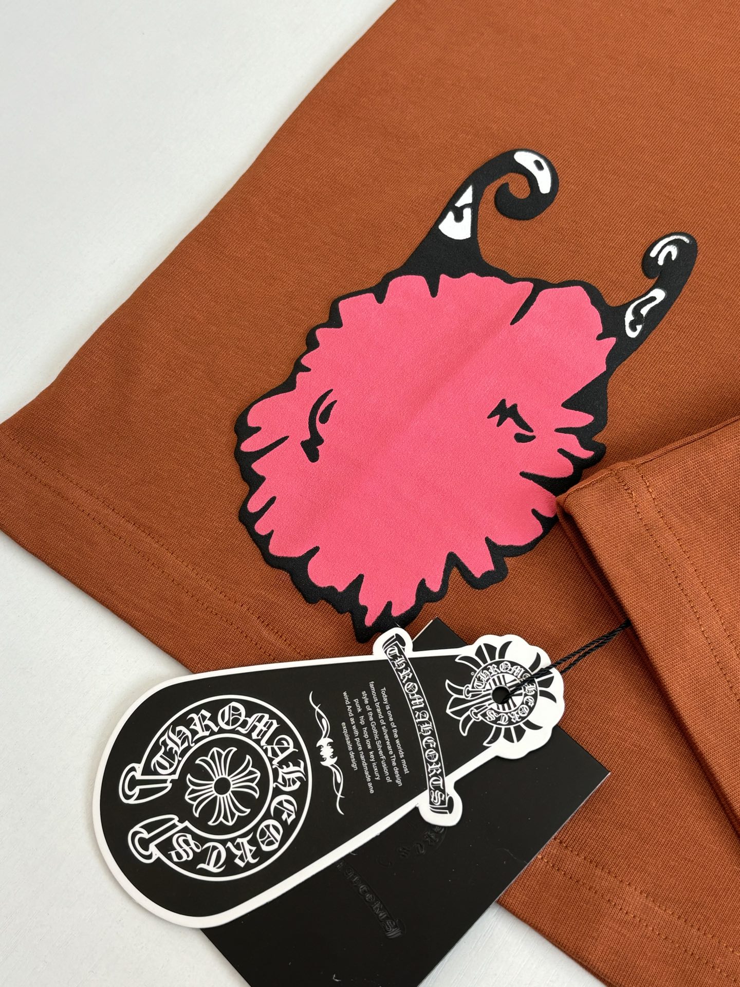 Orange T-shirt with large pink character graphic and attached black hang tag