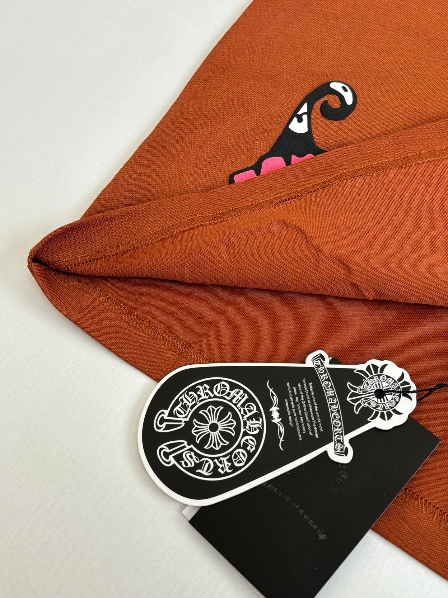 Orange T-shirt folded hem with pink character graphic and hanging hang tag