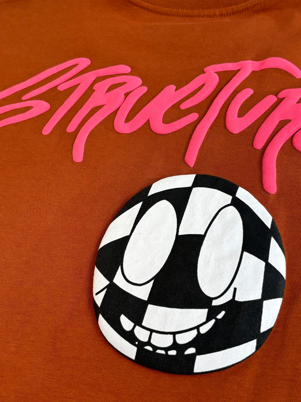 Orange T-shirt close-up with pink StreetLife script and black-and-white face graphic