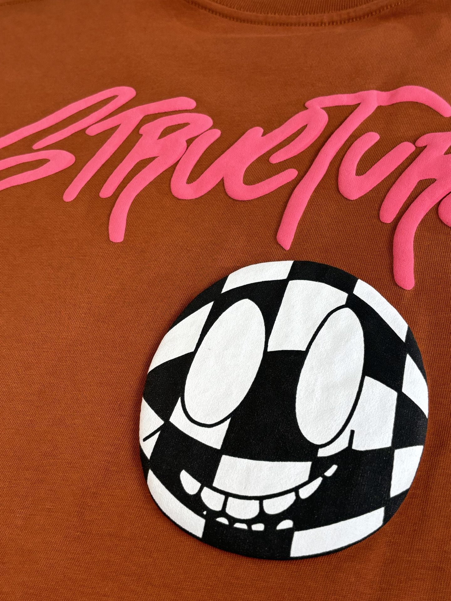 Orange T-shirt close-up with pink StreetLife script and black-and-white face graphic