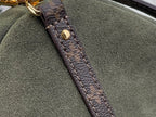 Louis Vuitton strap end detail: brown monogram tab with stitched border on olive bag