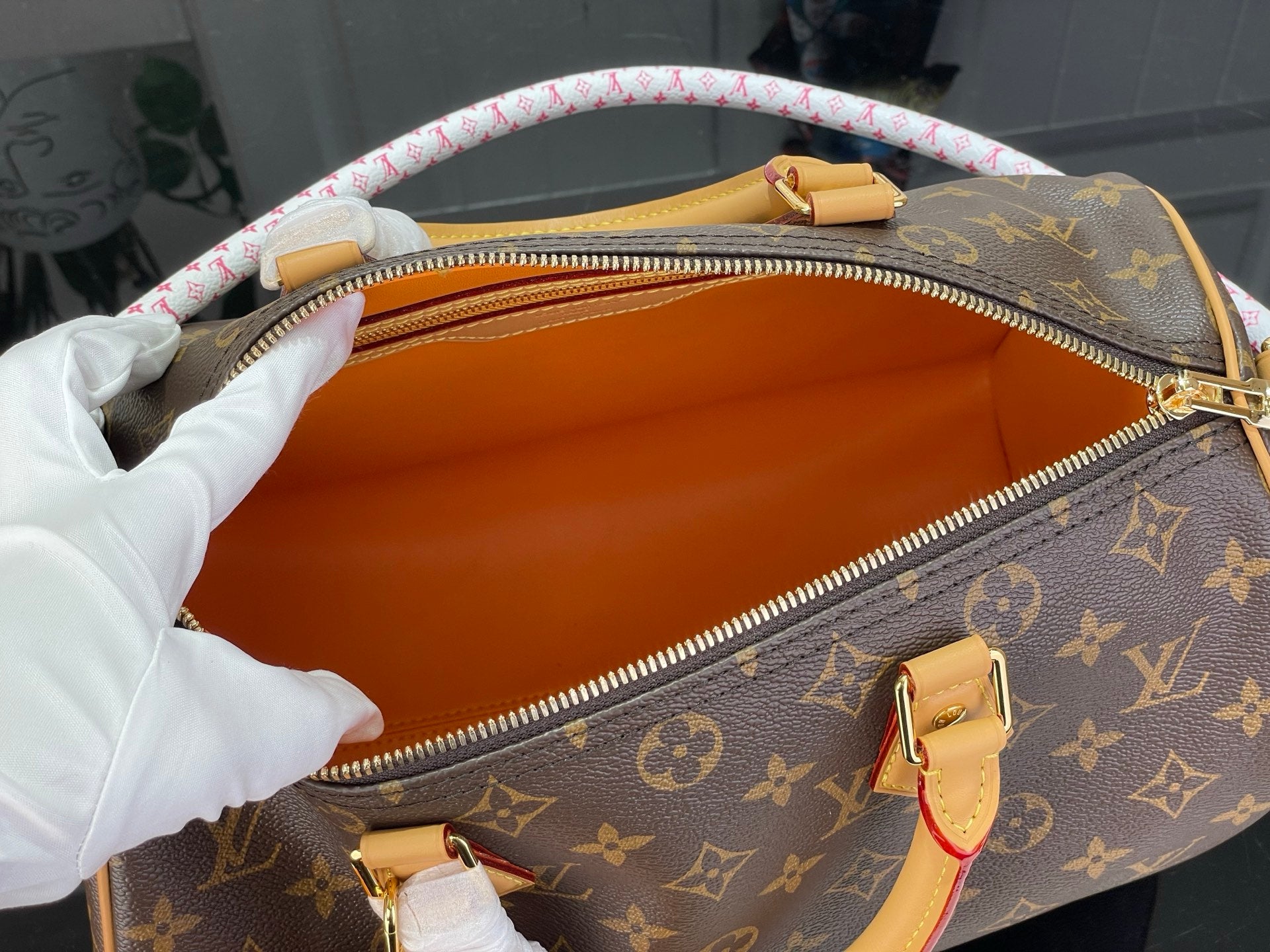 Monogram bag with open orange lining and gold zipper, tan handles