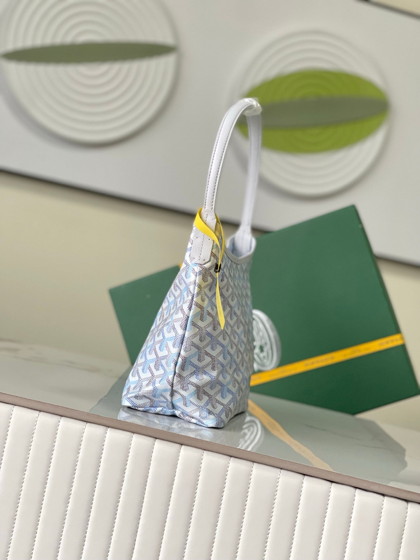 Light blue-and-white monogram hobo bag with long white handles and hanging yellow tag