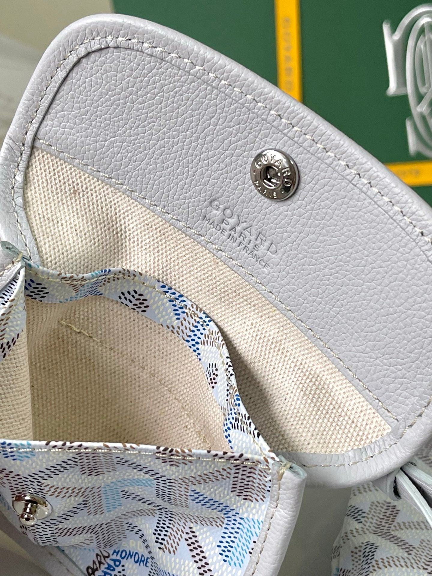 Light blue monogram bag end panel with white leather flap and round logo button