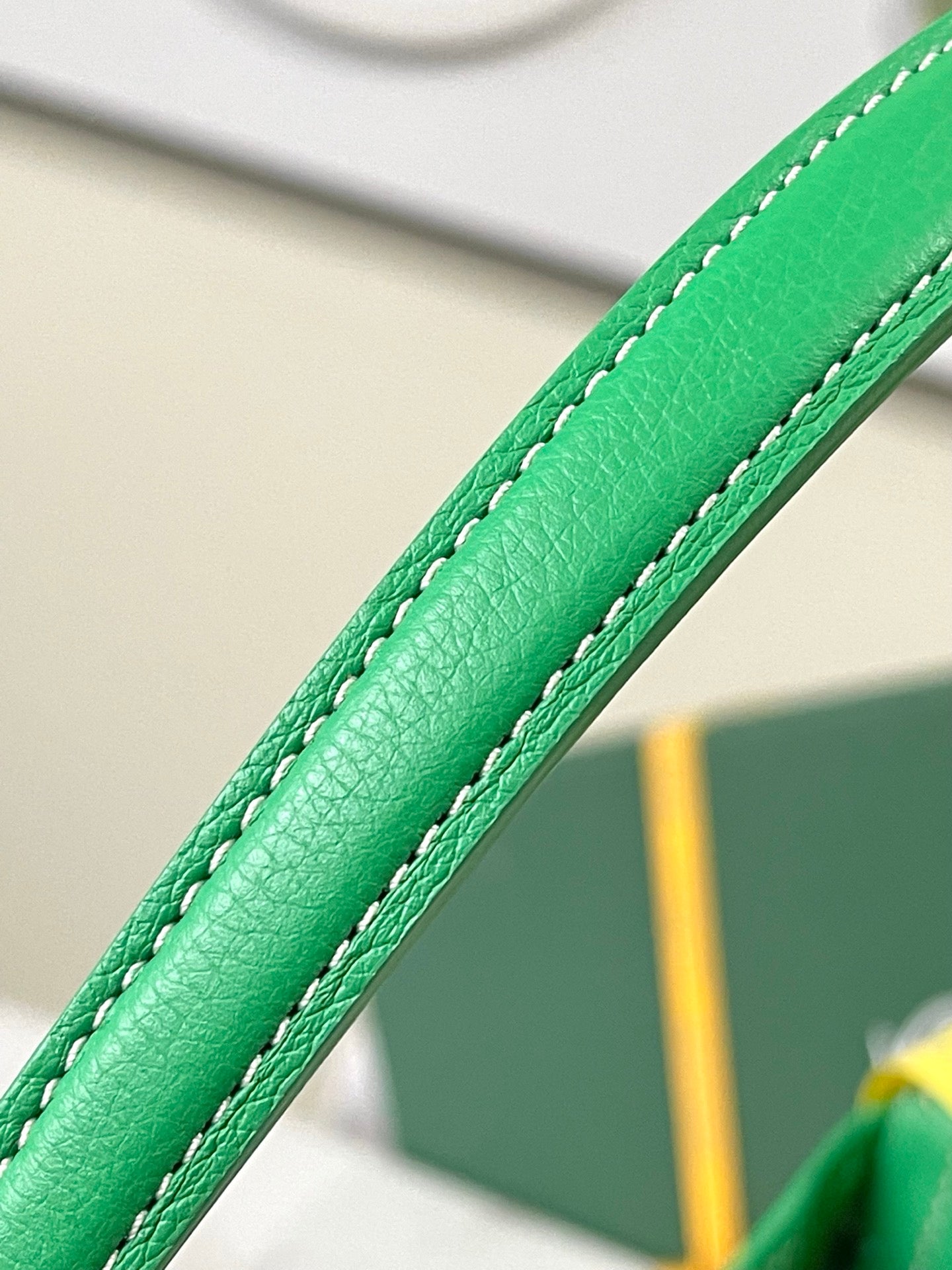 Green leather handle strap with stitched seam on a patterned bag.