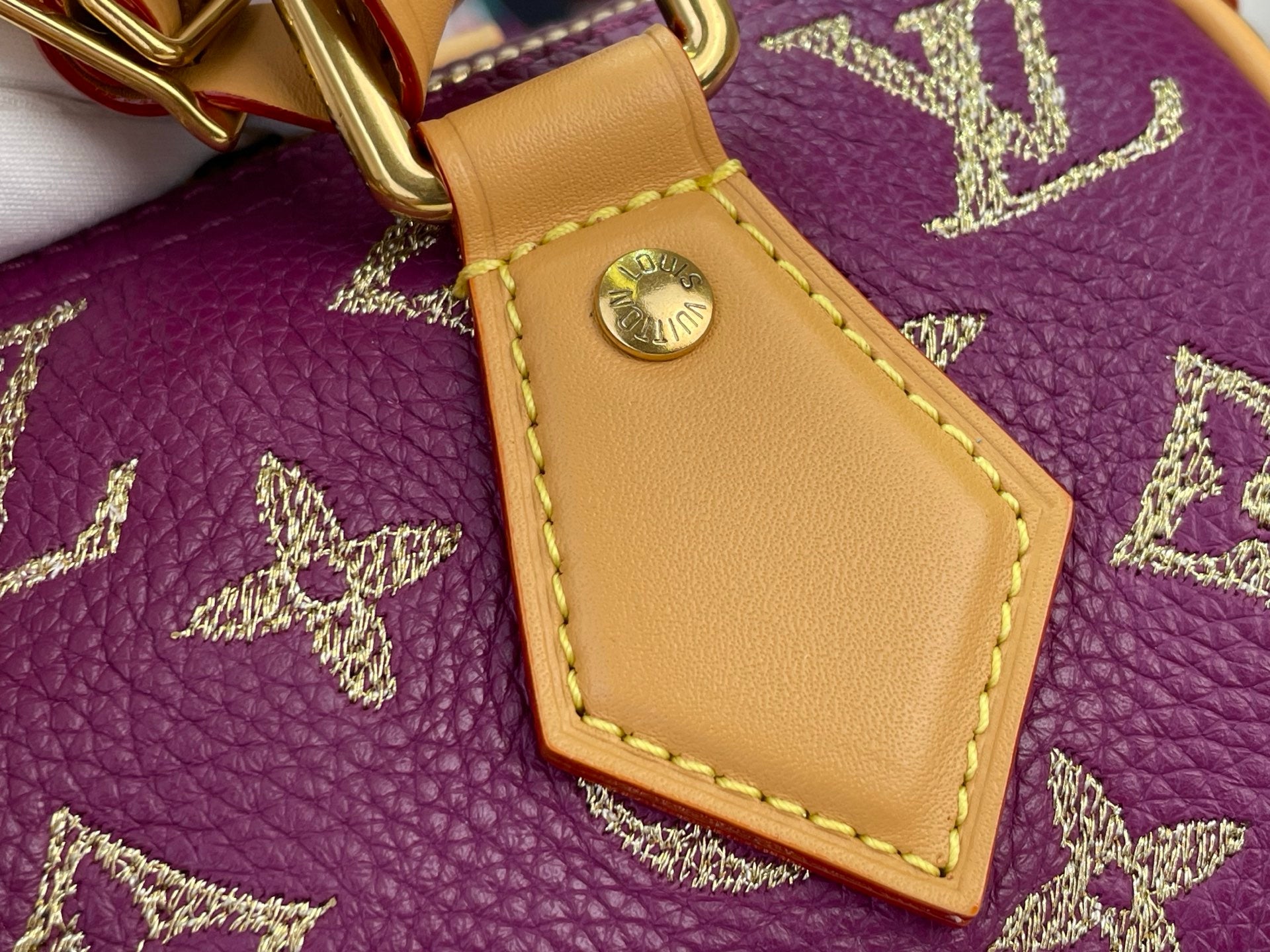 Louis Vuitton purple monogram handbag close-up of tan leather tab with gold rivet