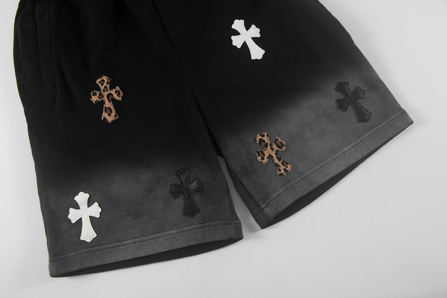 Black shorts with cross appliques along the hem, side-by-side leg view