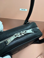 Black leather handbag side view with silver zipper hardware and front label patch.