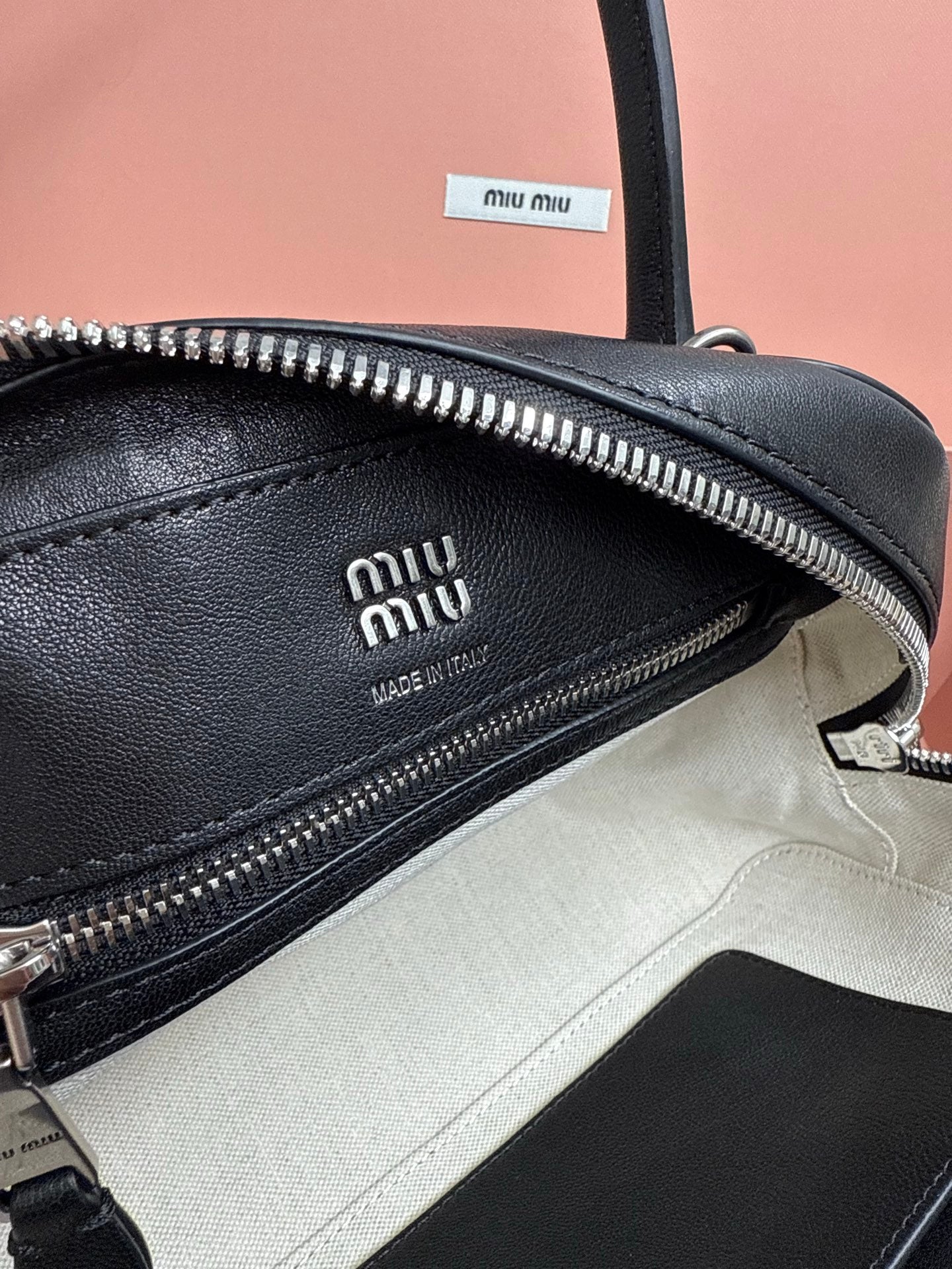 Black leather handbag interior close-up with embossed logo and silver zipper track.