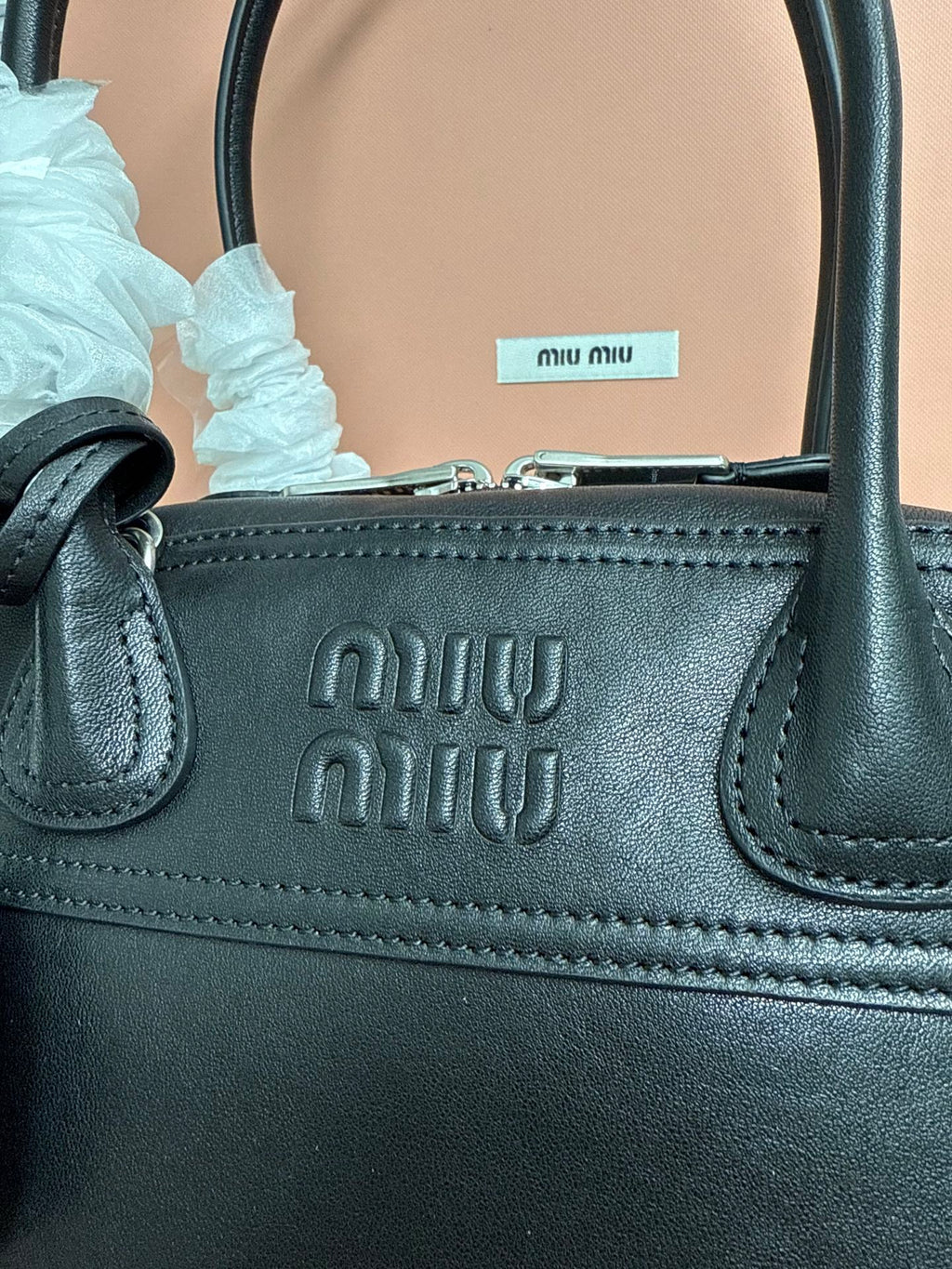 Black leather MiuMiu handbag with embossed logo on front and stitched handle base