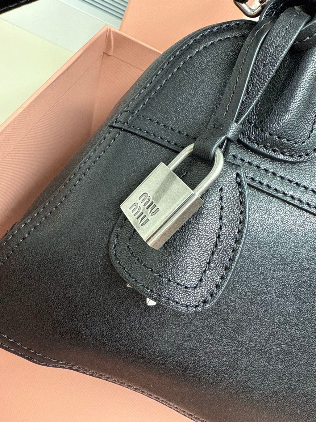 Black leather bag with silver padlock charm and logo tag on front strap
