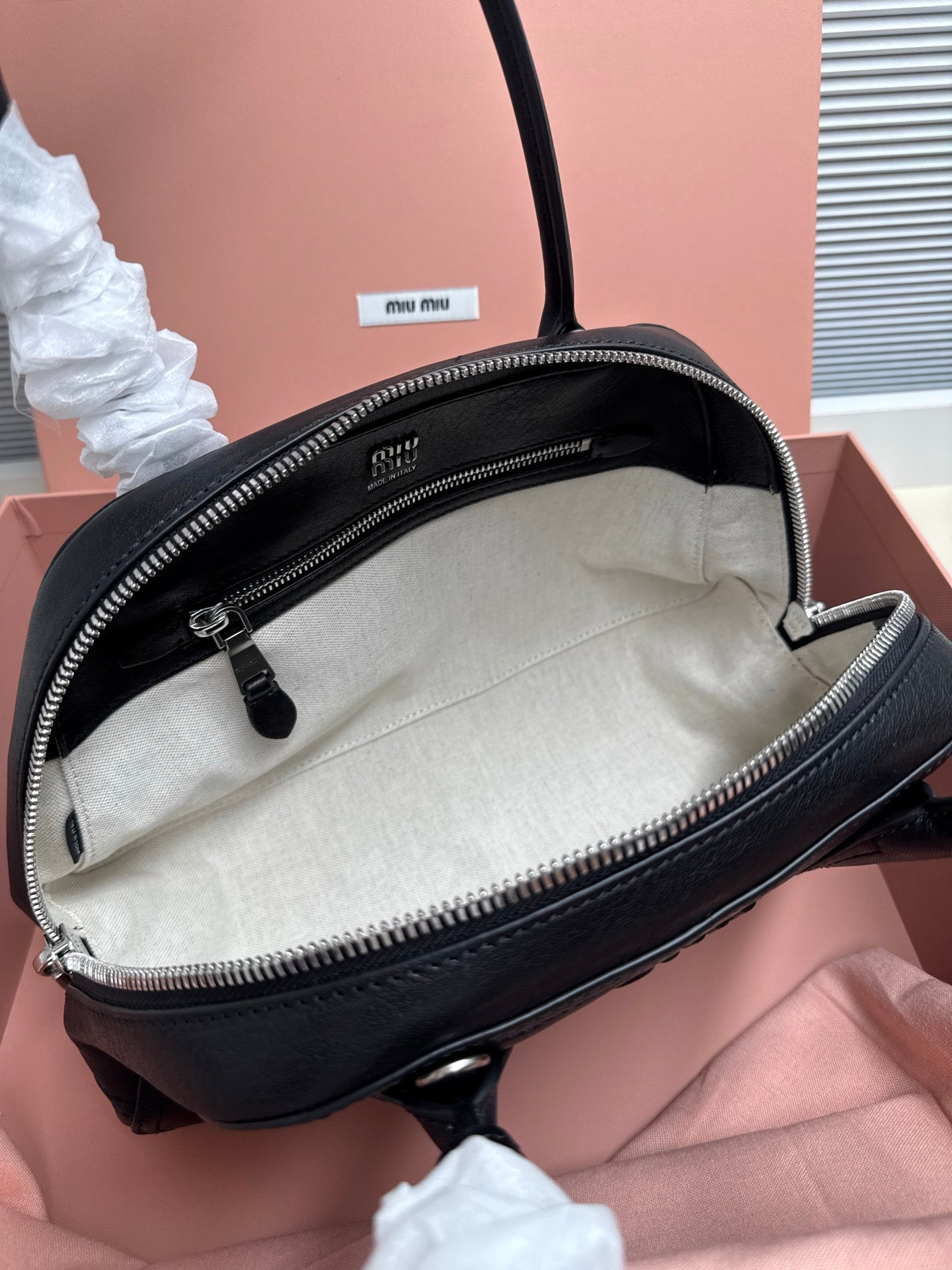 Black leather MiuMiu bag open at top, showing light interior and zipper closure