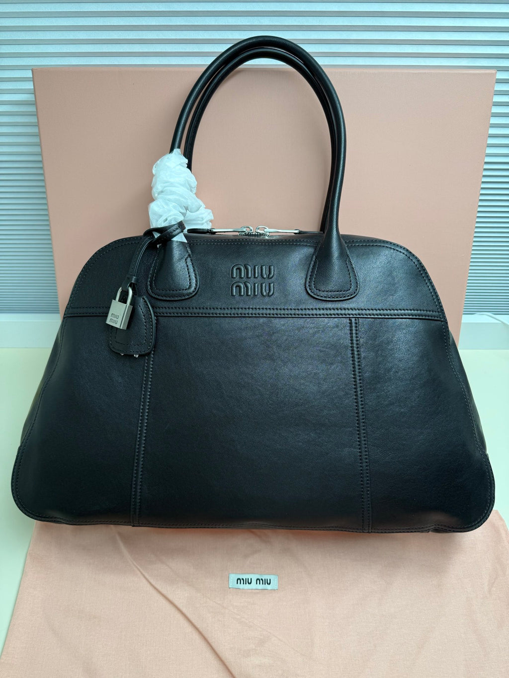 MiuMiu leather handbag with top handles, front logo, and charm detail