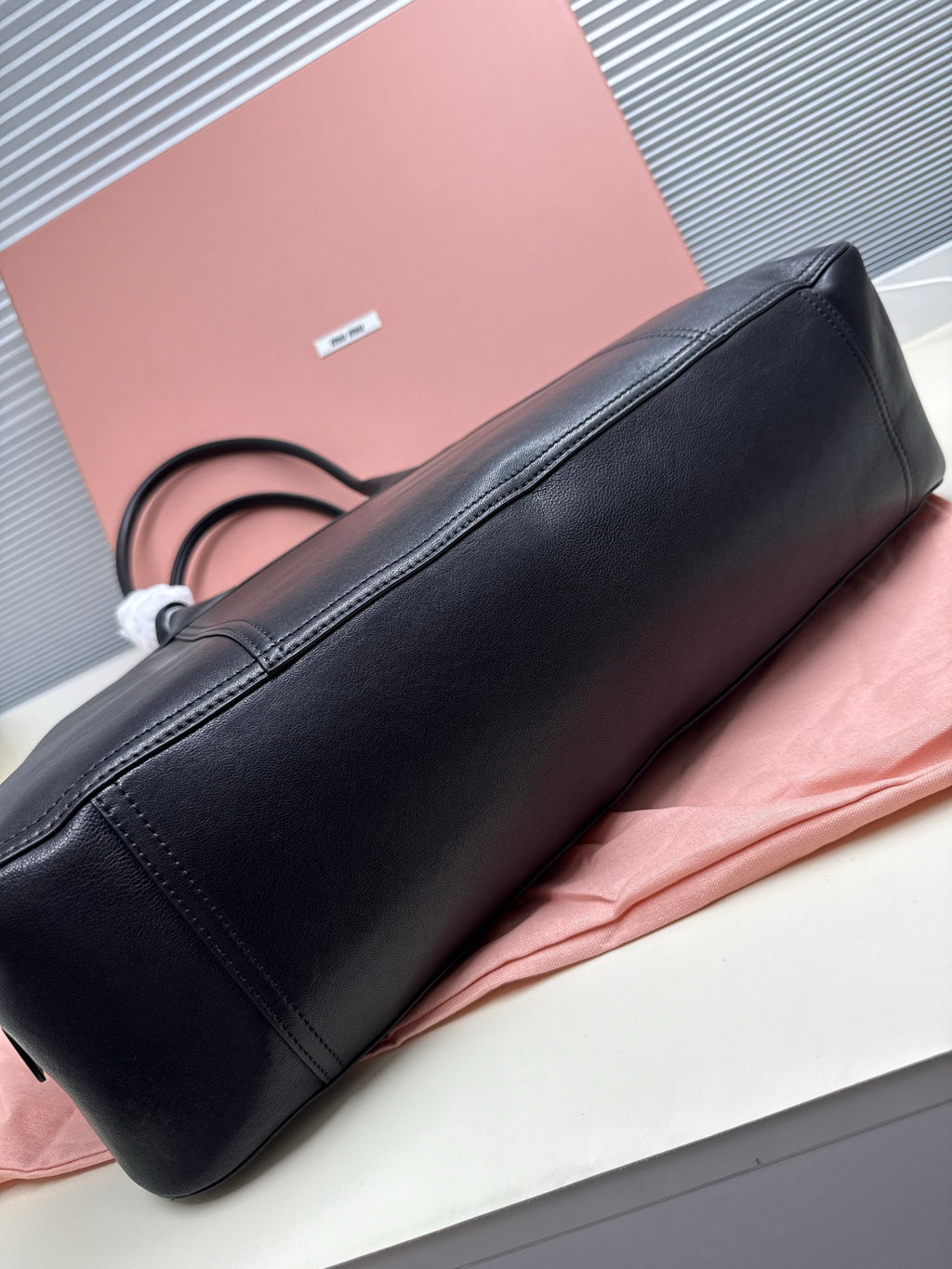 MiuMiu leather handbag side view on base with top handles and seams