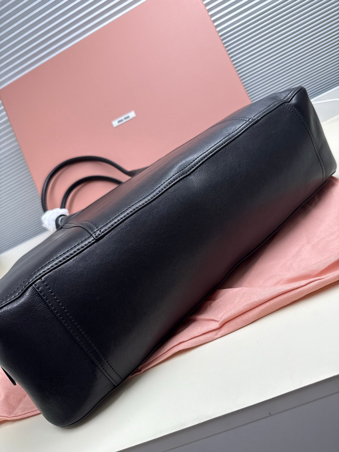 MiuMiu leather handbag side view on base with top handles and seams