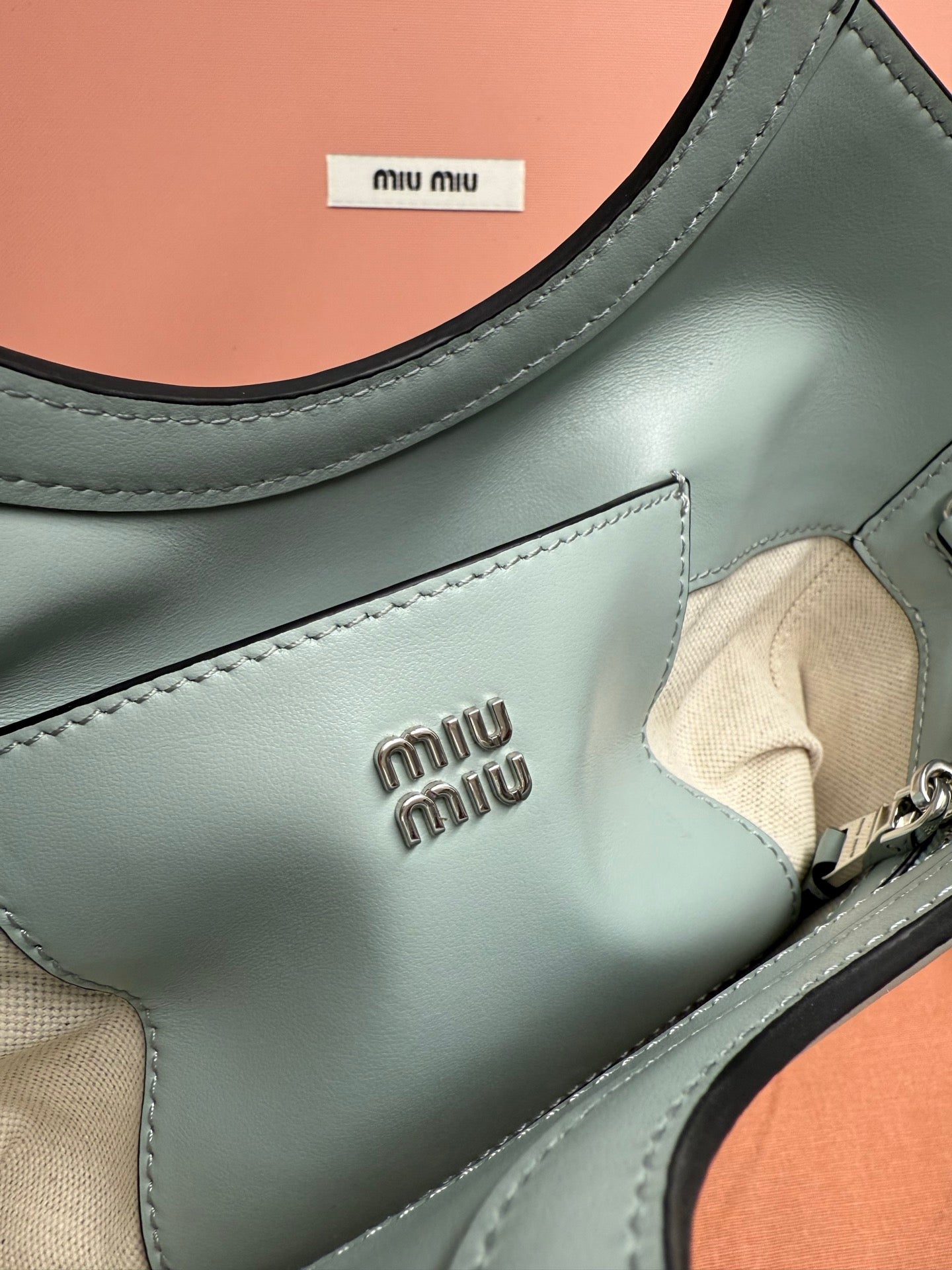 Miu Miu tote bag front pocket with embossed logo and beige fabric panel, close-up.