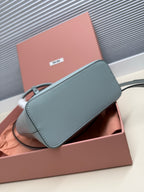 Miu Miu small teal leather bag with black strap and top flap, side view.