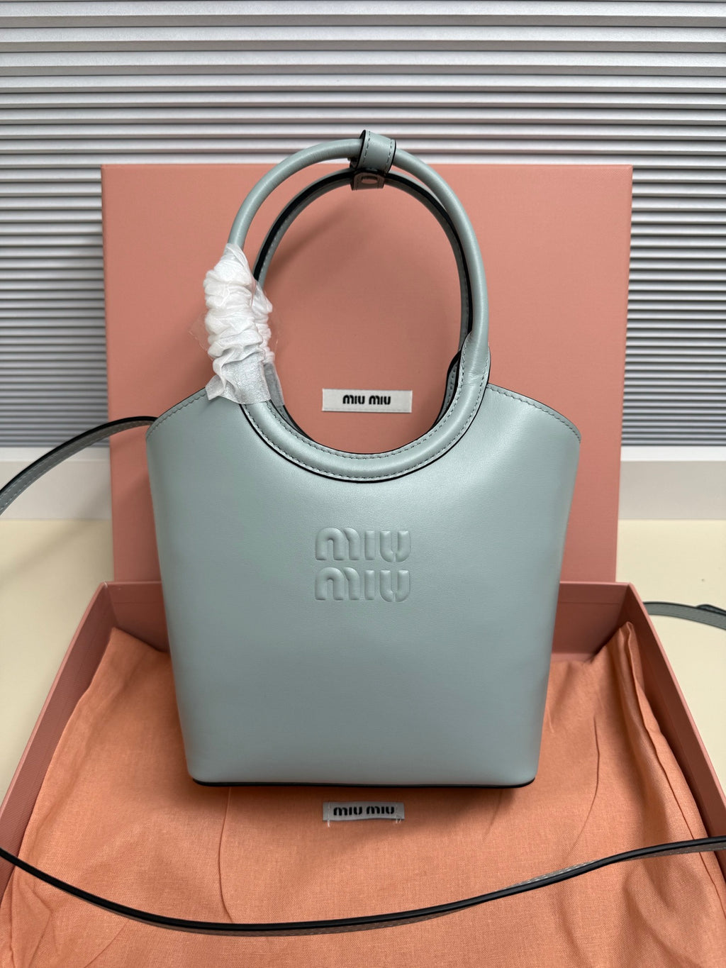 Miu Miu mini tote bag in light teal leather with wrapped top handle and embossed logo.