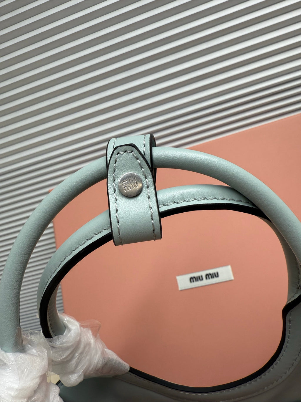 Miu Miu tote bag handle attachment in light teal leather with metal hardware, close-up.