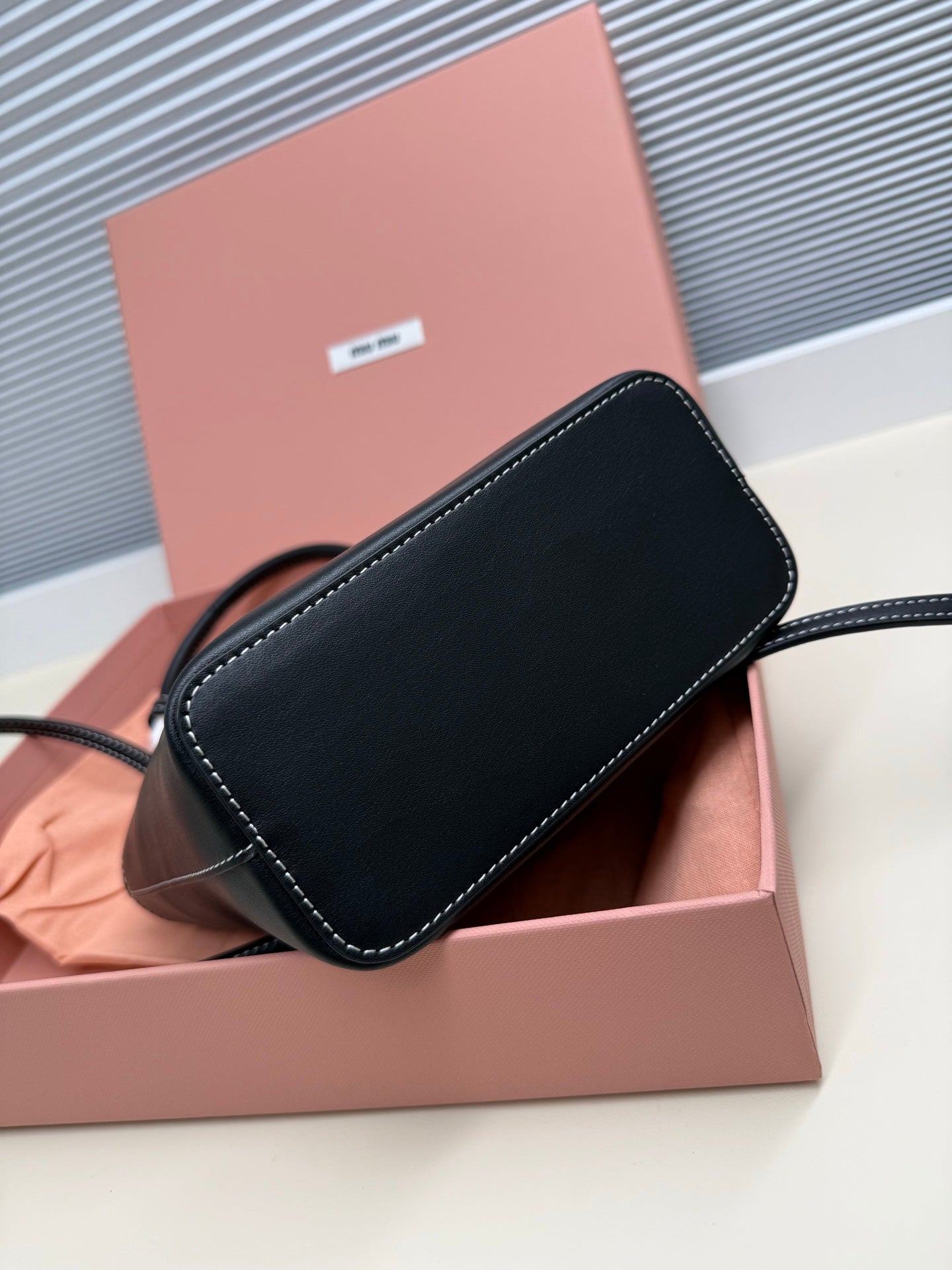 Black leather Miu Miu mini crossbody pouch with stitched edges and attached strap.