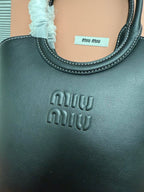 Green-toned leather Miu Miu handbag close-up of curved handle base and embossed logo.
