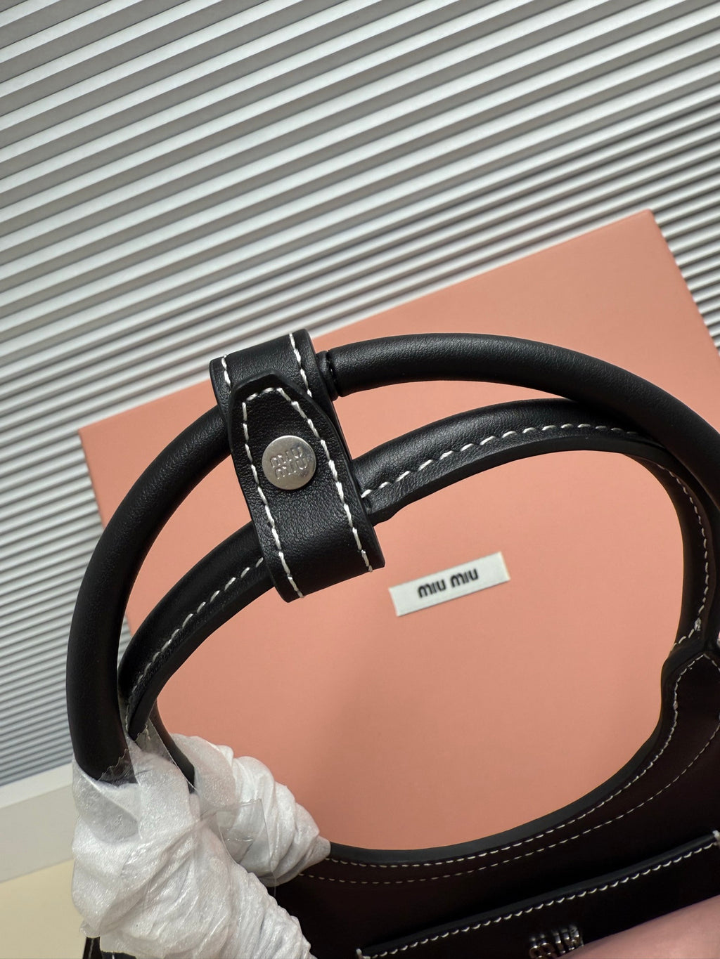 Black leather Miu Miu handbag close-up of handle strap with metal ring and stitched edge.