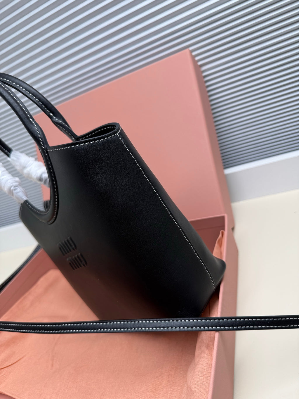 Black leather Miu Miu handbag shown from the side with stitched details.