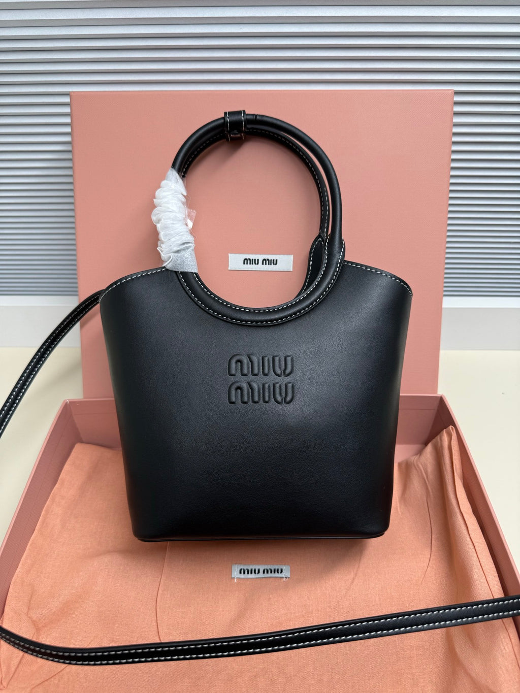 Black leather Miu Miu handbag with curved top handles and embossed logo on front.