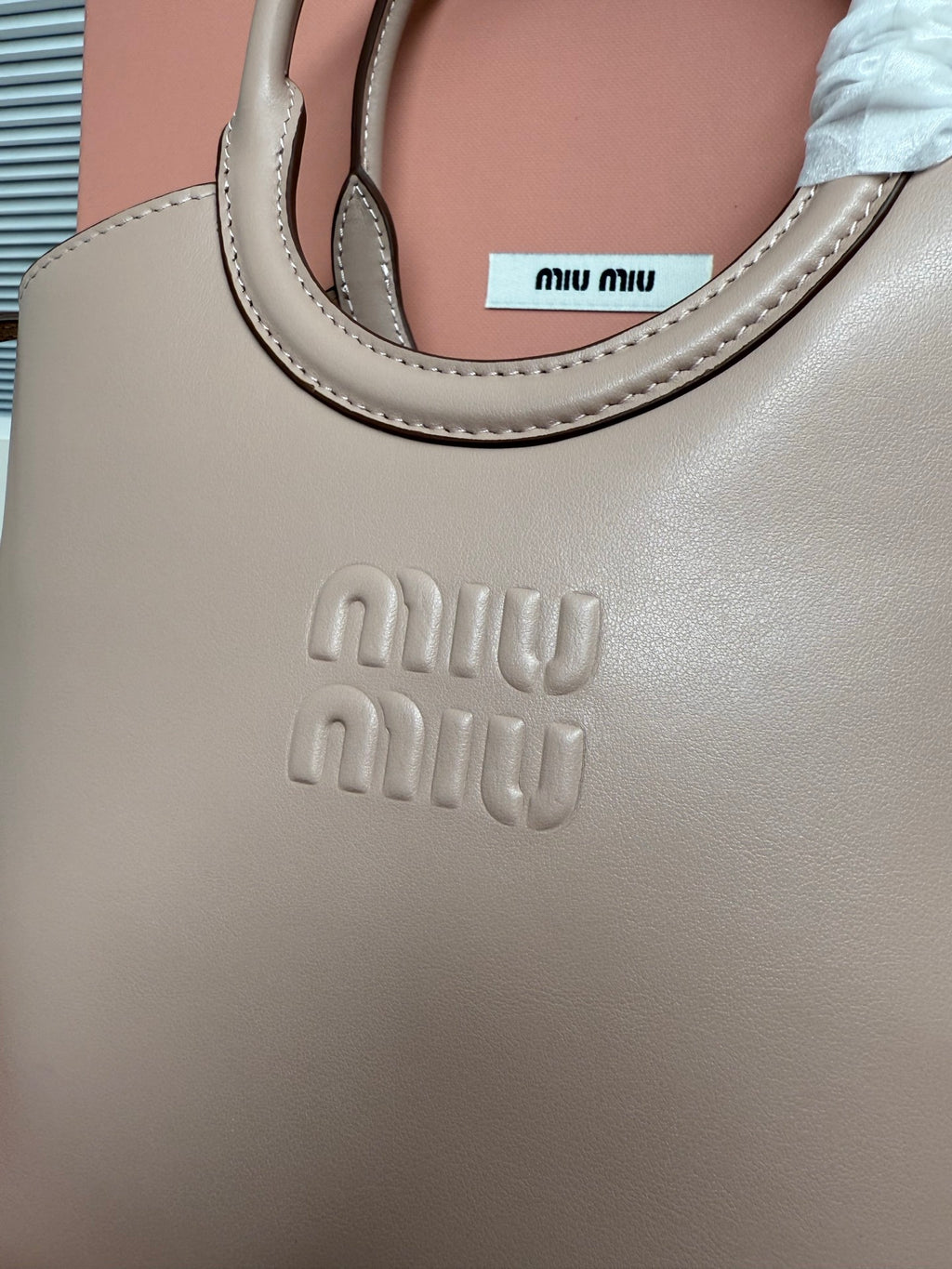 MiuMiu tote bag close-up: embossed “miu miu” logo on light gray leather
