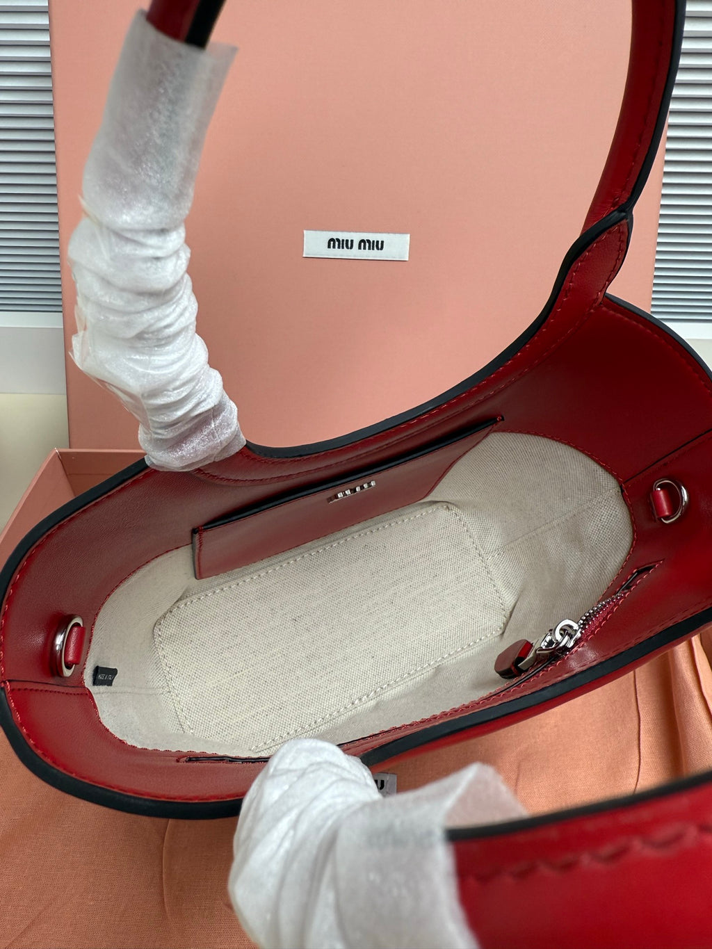 Open red leather Miu Miu bag showing light canvas interior and stitched inner edge