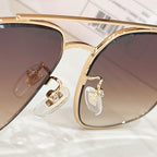 Gold sunglasses frame with clear lens area and decorative logo detail on temple
