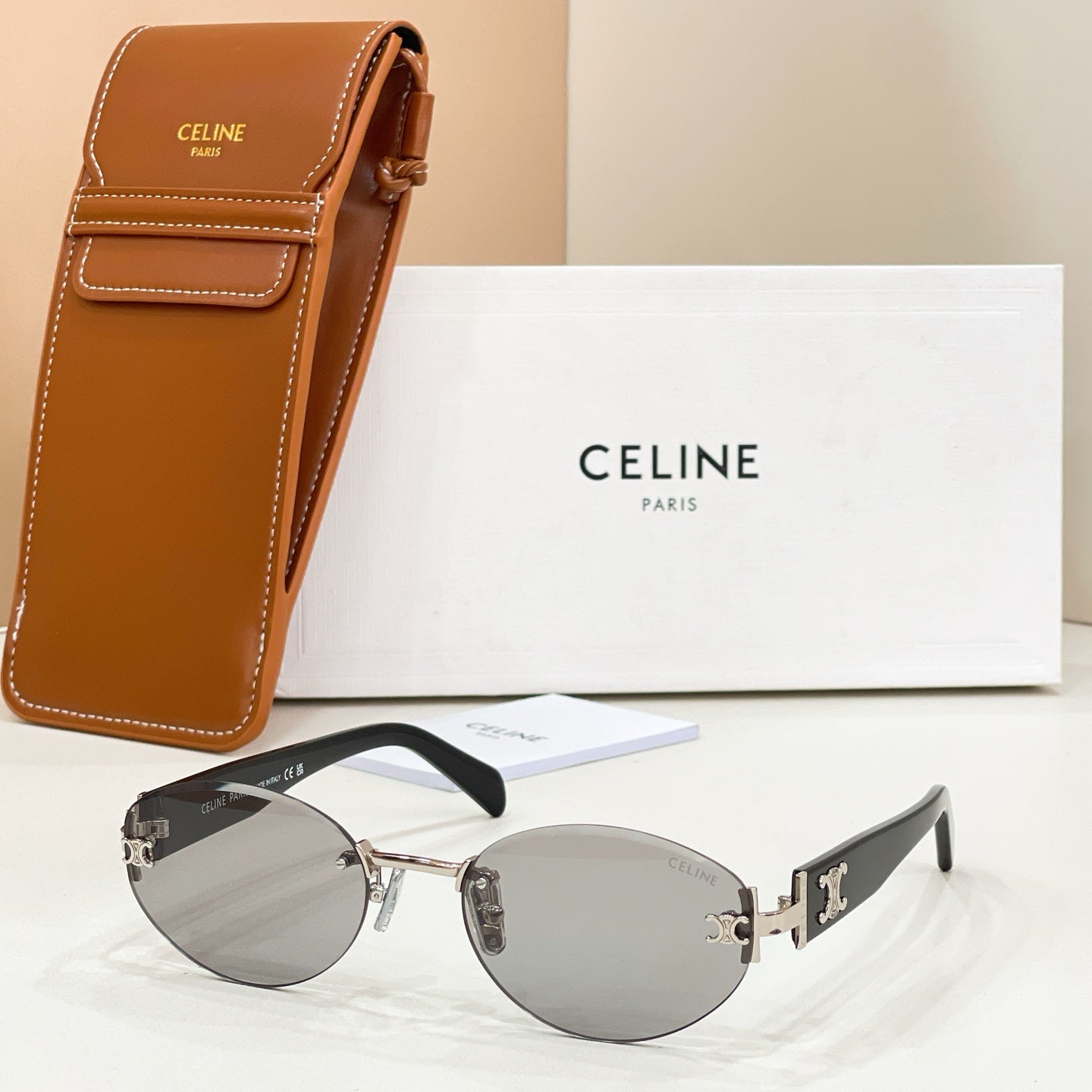 Cat-eye sunglasses with gold frame, gray tinted lenses, and black temples with gold logo detail.