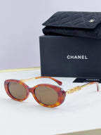 Chanel round sunglasses with orange-red frames and tinted lenses, gold chain temple detail.