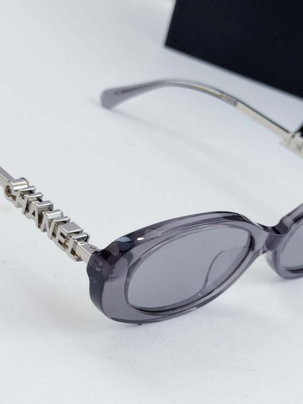 Chanel oval sunglasses with dark lenses; metal chain detail and clear frame temples.