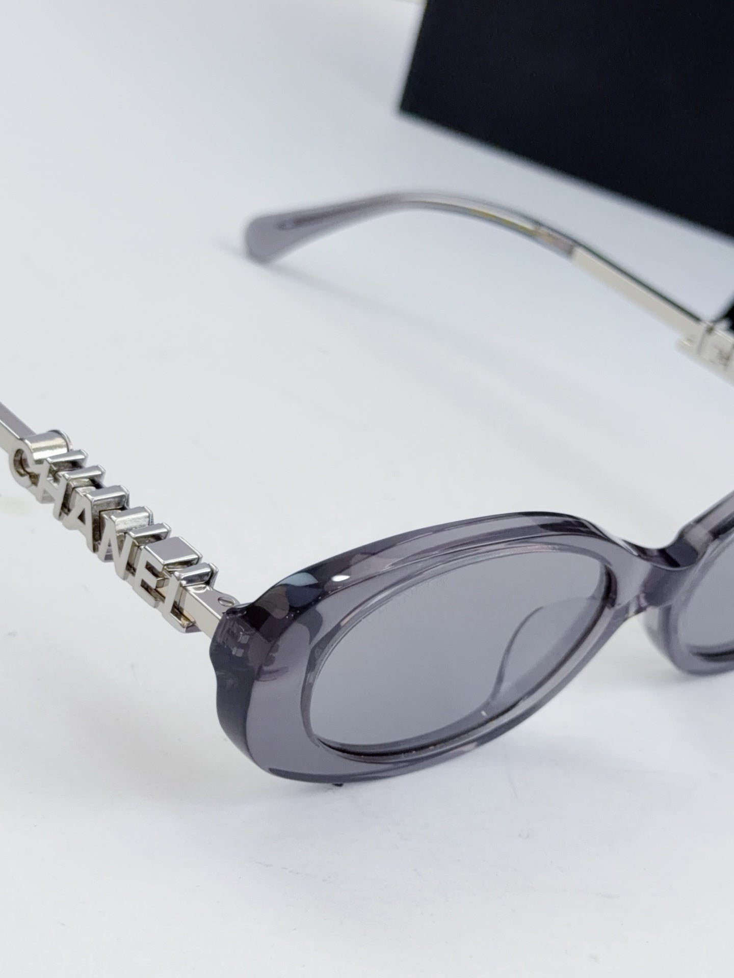 Chanel oval sunglasses with dark lenses; metal chain detail and clear frame temples.