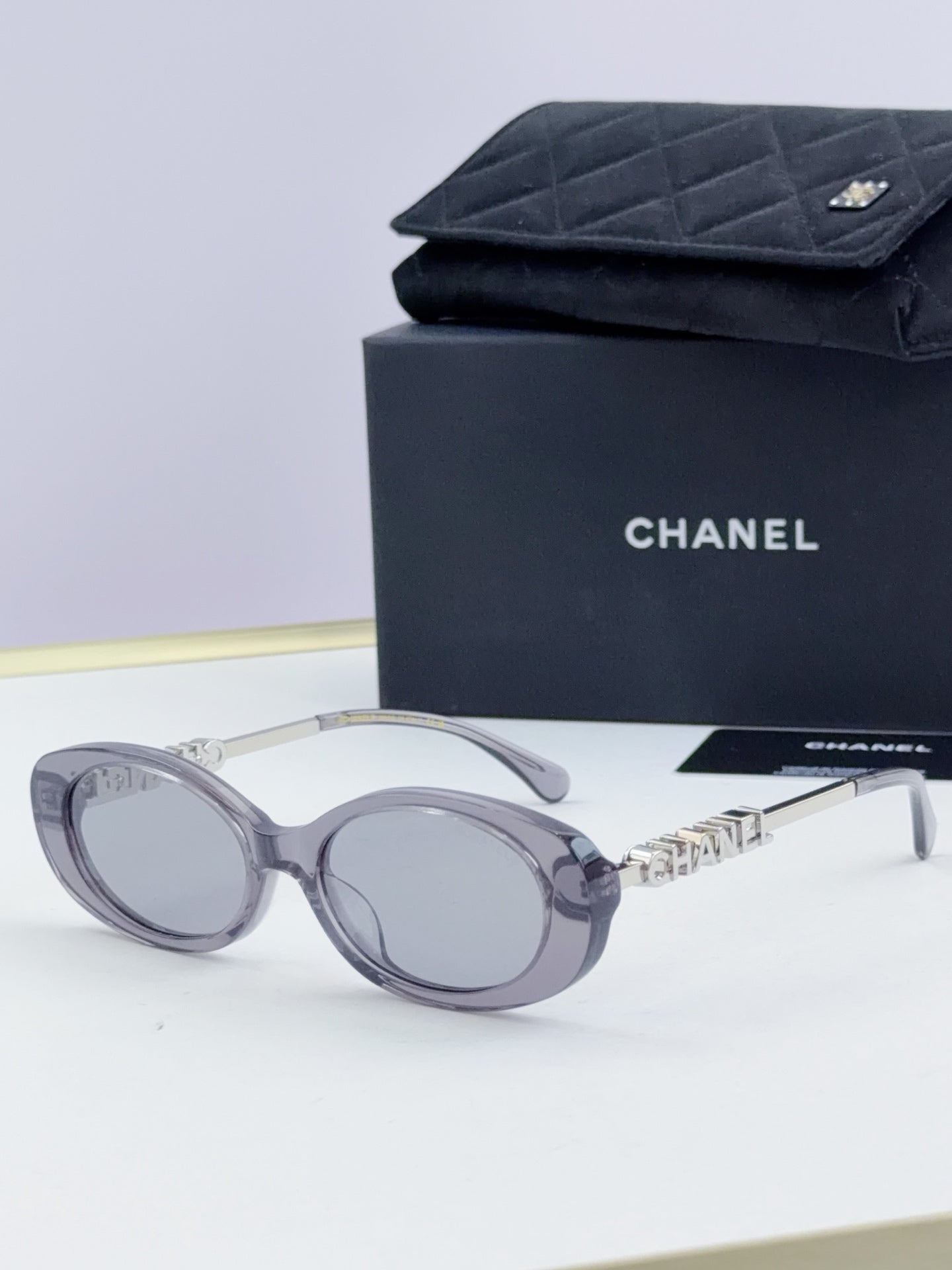 Chanel round sunglasses with clear-gray frames and tinted lenses, gold chain temple detail.