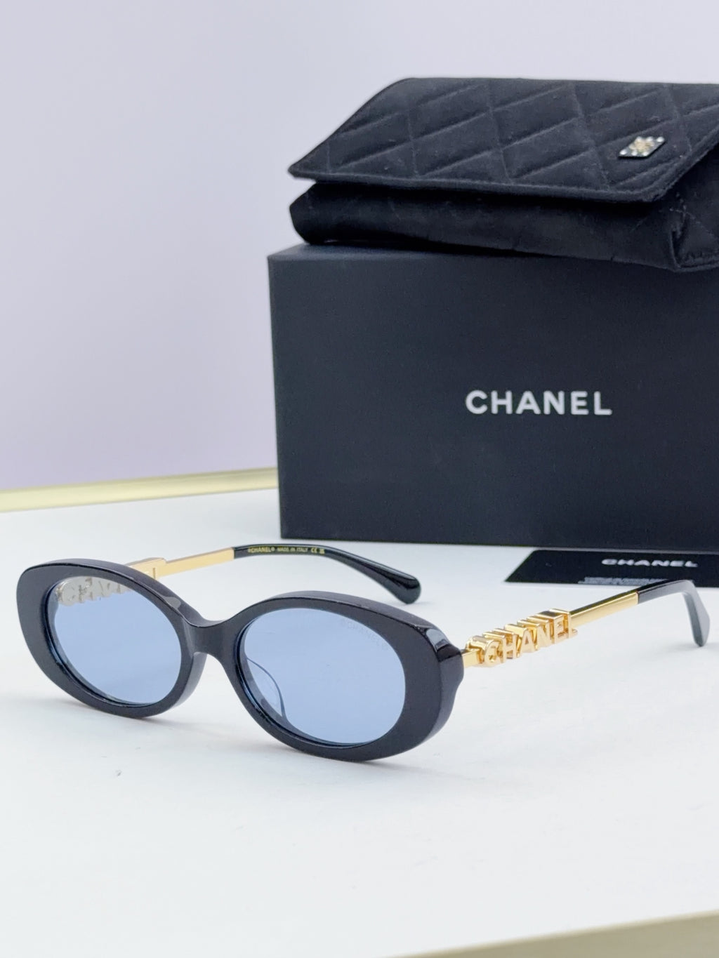 Chanel round sunglasses with navy frames and blue-tinted lenses, gold chain temple detail.