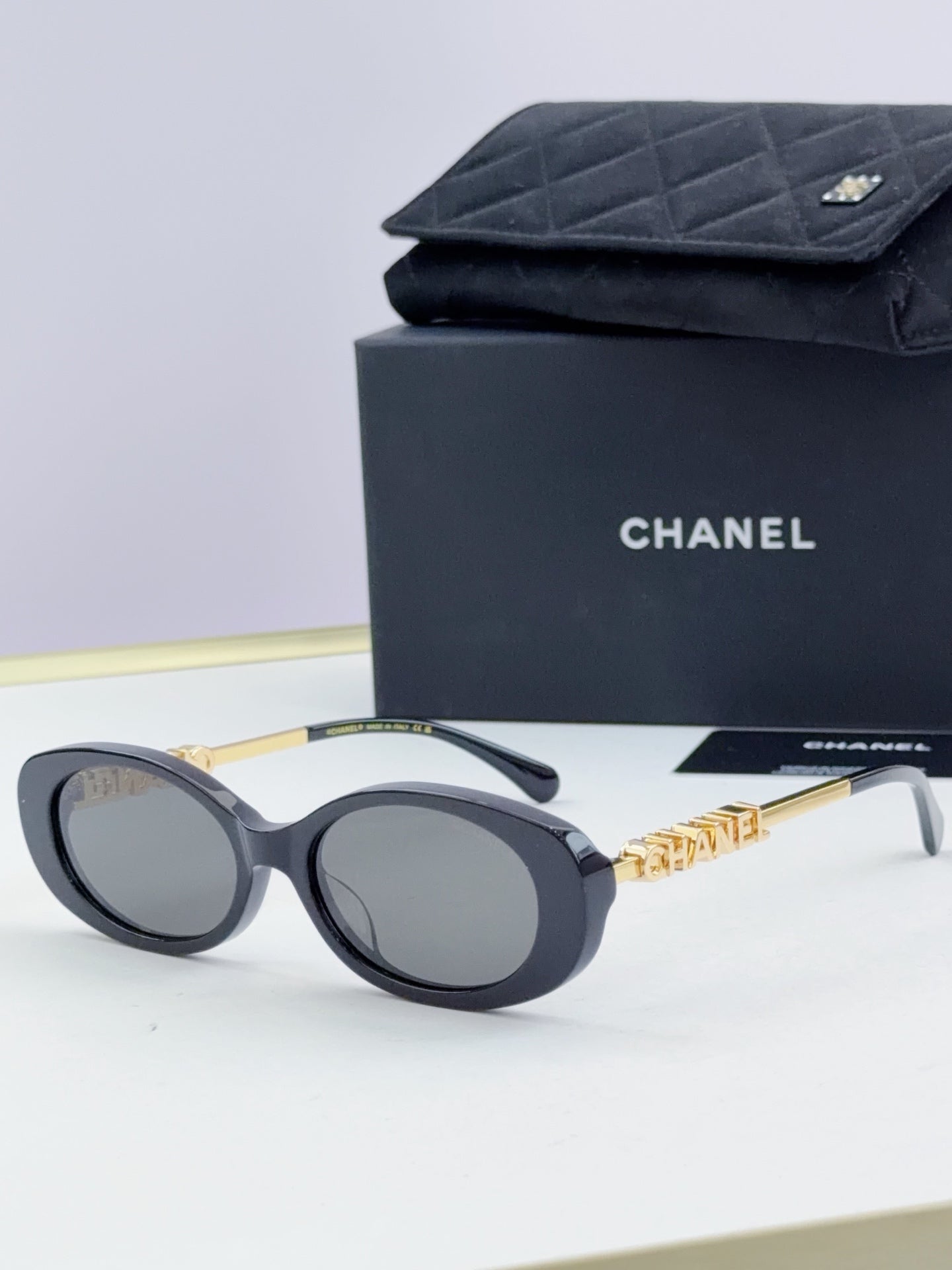 Chanel round sunglasses with dark lenses and black frames, gold chain detail on temples.
