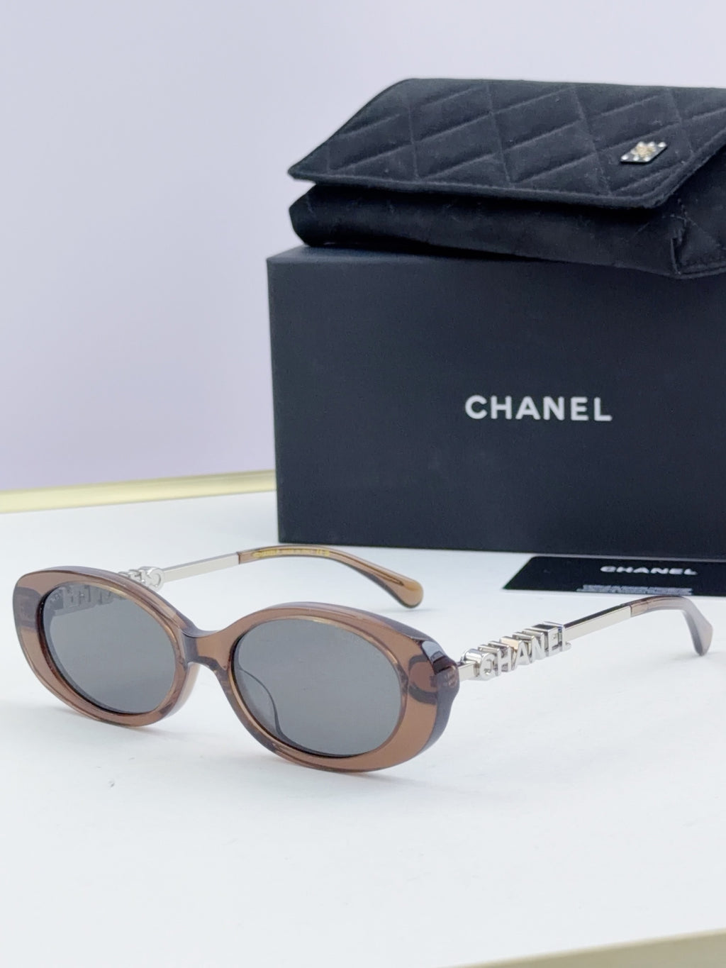Chanel round sunglasses with light brown frames and tinted lenses, gold chain temple detail.
