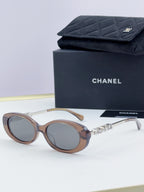 Chanel round sunglasses with light brown frames and tinted lenses, gold chain temple detail.