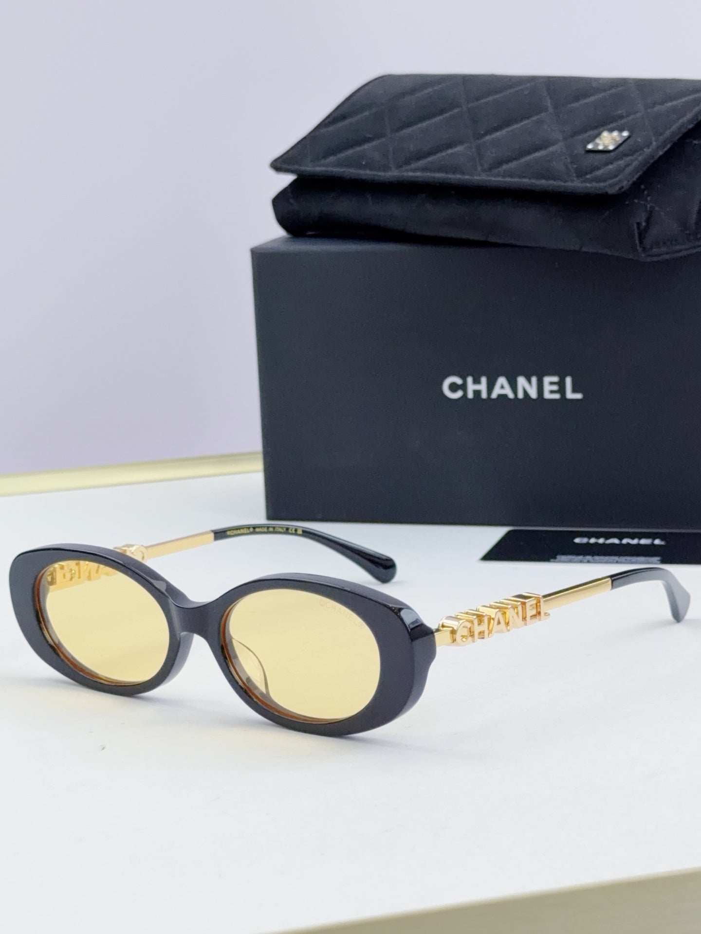 Chanel round sunglasses with dark frames and yellow-tinted lenses, gold chain detail.