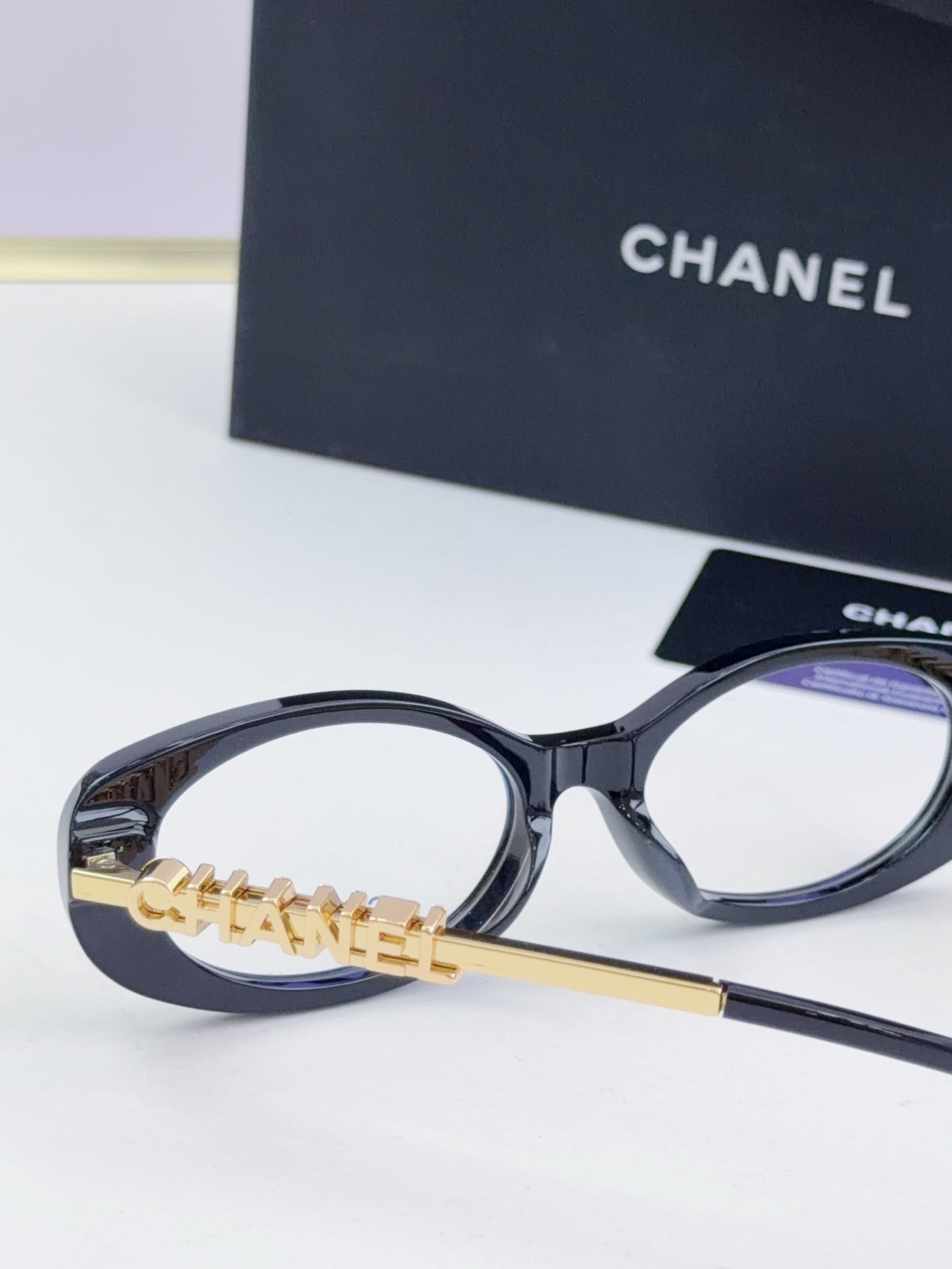 Chanel eyeglasses side view: dark round frame with gold-tone chain temple logo and clear lenses.