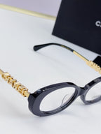 Chanel eyeglasses detail: dark frame with gold-tone chain temple logo and clear lenses.