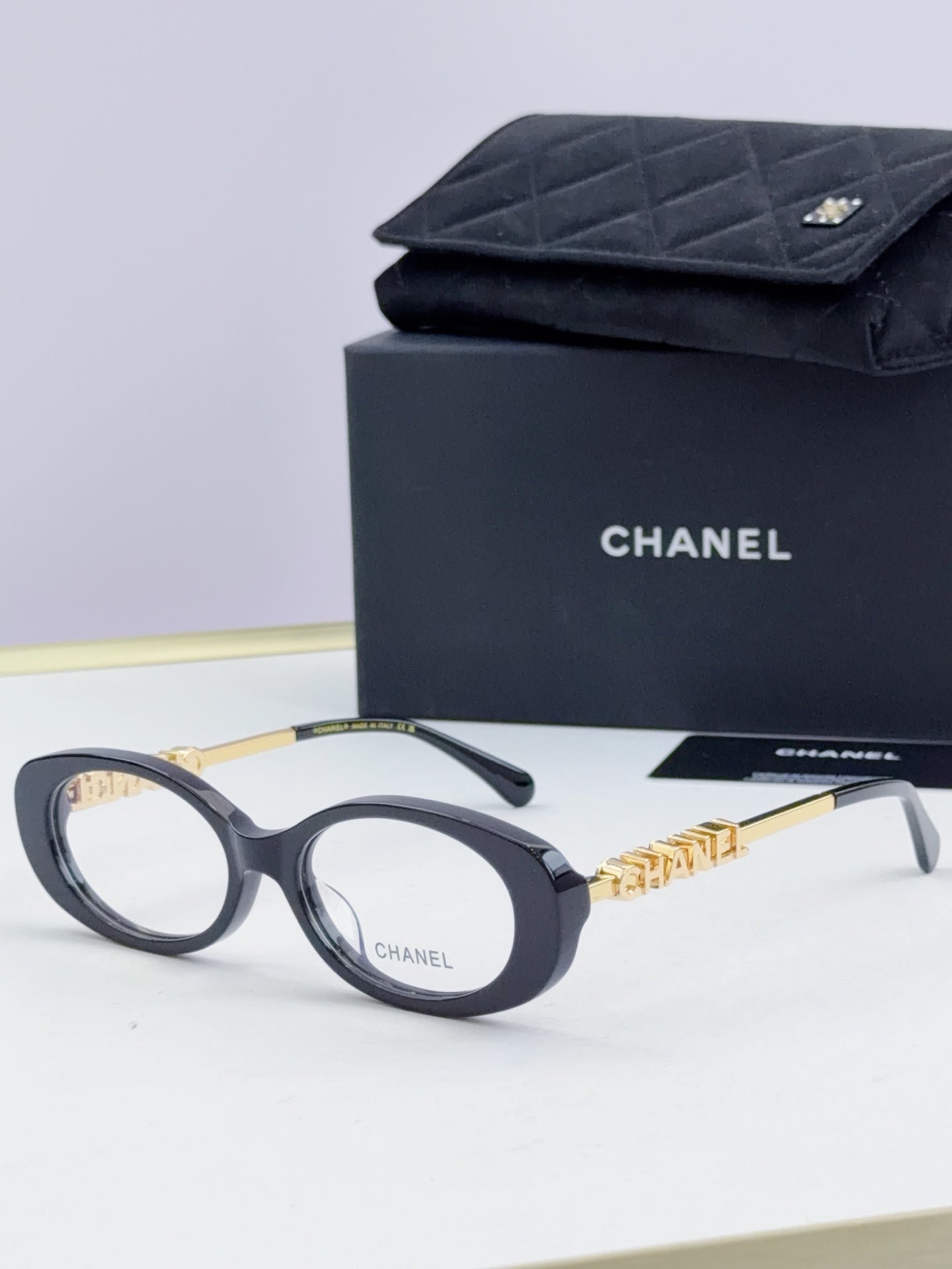 Chanel eyeglasses with dark frame, gold-tone logo temples, and clear lenses; with case.